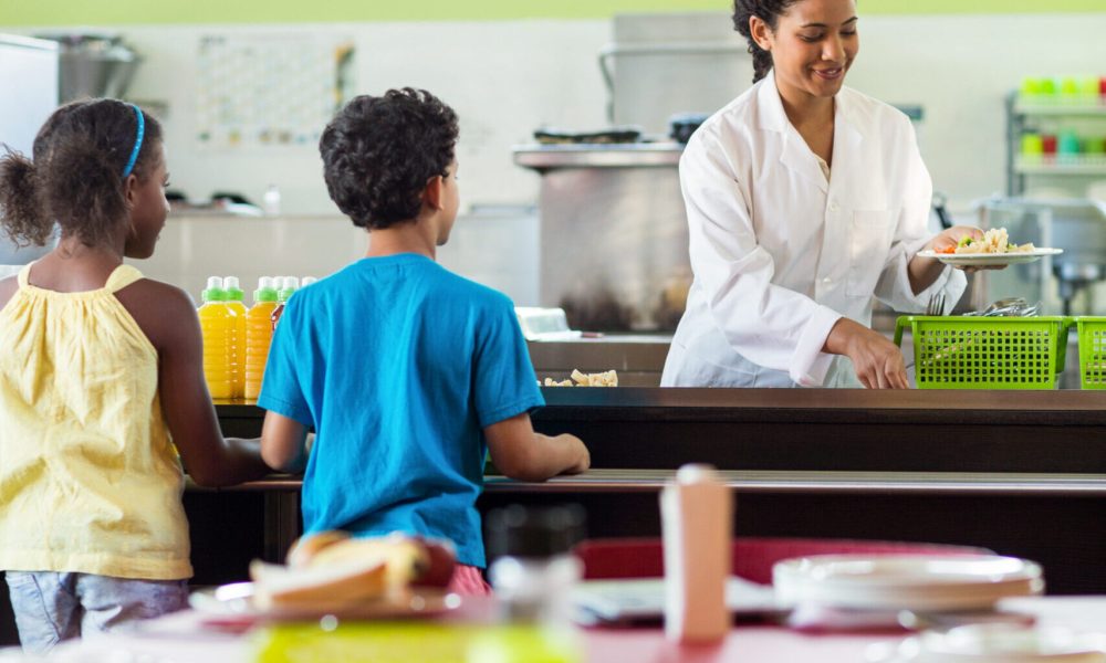 Woman serving food to schoolchildren in canteen